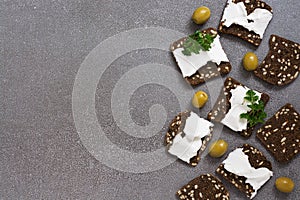 Black toasted bread with cheese and grains on a gray surface. View from above.