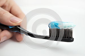 Black toothbrush with the minty color of toothpaste in the girl`s hand