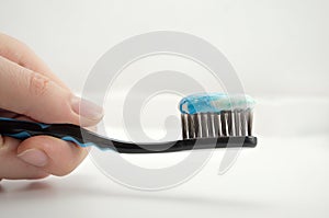 Black toothbrush with the minty color of toothpaste in the girl`s hand