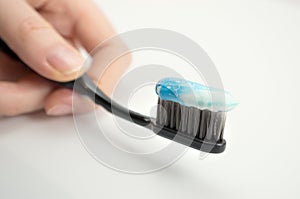 Black toothbrush with the minty color of toothpaste in the girl`s hand