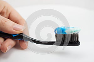 Black toothbrush with the minty color of toothpaste in the girl`s hand