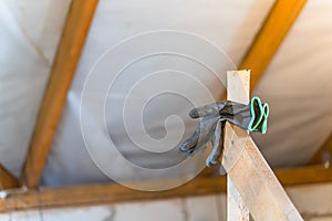 Black torn construction rubberized gloves hang against the background of an uninsulated roof