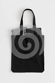 Black tote bag mockup with notebooks on a white table