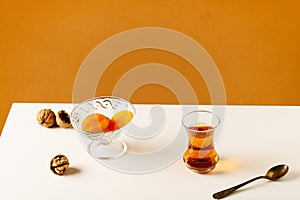 Black traditional Turkish tea in a glass cup and dried fruits on a white table.