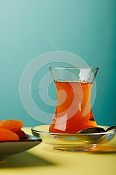 Black traditional Turkish tea in a glass cup and dried fruits on a white table.