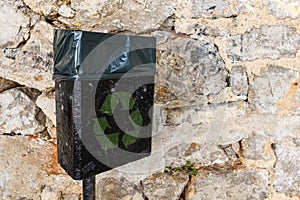 Black trash can with green recycling symbol on the street