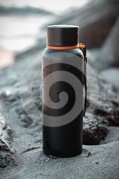 a black, travel water bottle sitting on a beach near the ocean