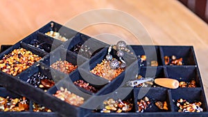 A black tray for handcrafting with multiple sections filled with various kinds of amber and tools for crafting