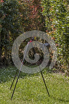 A black tripod with a removable cross column is placed in a lawn to photograph flowers and insects up close in a stable manner