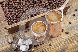 Black Turkish coffee in copper cup and roasted coffee beans scattered on wooden table. Traditional Turkish coffee in copper cup
