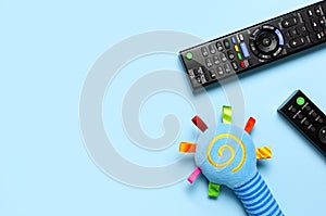 Black TV audio remote control and baby toys rattles, toy puppy on blue background flat lay top view copy space. Concept of viewing