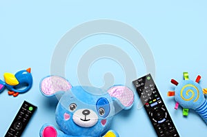 Black TV audio remote control and baby toys rattles, toy puppy on blue background flat lay top view copy space. Concept of viewing