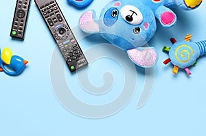 Black TV audio remote control and baby toys rattles, toy puppy on blue background flat lay top view copy space. Concept of viewing