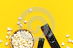 Black TV, audio remote control and popcorn on bright yellow background flat lay top view copy space. Minimalistic background with