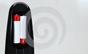 Black TV remote control with AAA alkaline batteries in red and white on a white background. Battery replacement, spare parts.