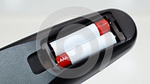 Black TV remote control with AAA alkaline batteries in red and white on a white background. Battery replacement, spare parts.