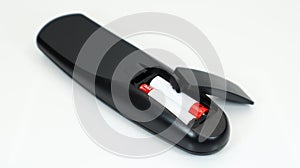 Black TV remote control with AAA alkaline batteries in red and white on a white background. Battery replacement, spare parts.