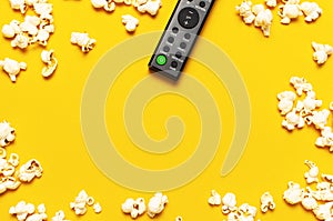 Black TV remote control and popcorn on bright yellow background flat lay top view copy space. Minimalistic background with a