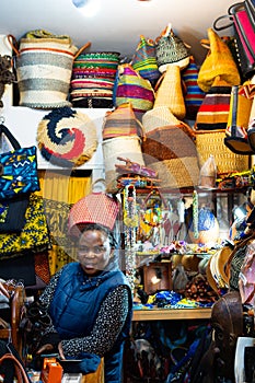 black Ugandan woman in her small store surrounded by handbags and souvenirs, looking at the camera