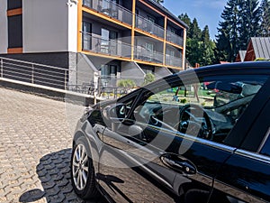 A black unrecognizable modern car parked in front of modern houses with balconies or relaxation center