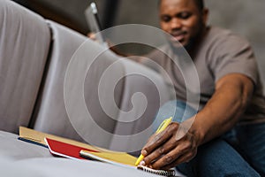Black unshaven man using tablet computer while writing down notes
