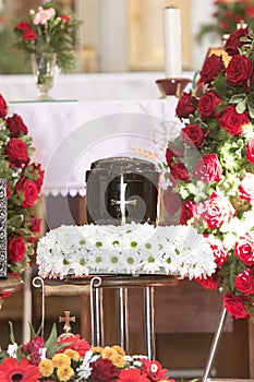 Black urn on the funeral day in church; surrounded with daisies and roses