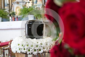 Black urn on the funeral day in church; surrounded with daisies and roses