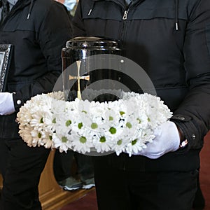 Black urn on the funeral day in church; surrounded with daisies and roses