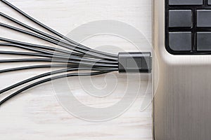 Black USB cables connected to laptop on white wooden background
