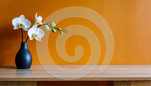 Black vase with an white orchid on wooden table near a blank orange wall. Empty space for text.