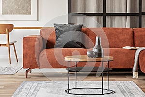 Black vase on wooden coffee table in chic living room interior with comfortable sofa