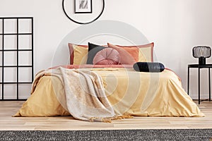 Black velvet pillow on yellow duvet in trendy bedroom interior with king size bed