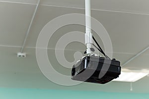 The black video projector is suspended from a long bracket under the ceiling.