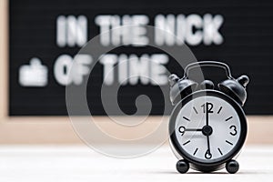 black vintage alarm clock on the background of signs with the inscription in the nick of time