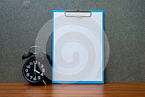 Black vintage alarm clock with clipboard and blank white paper,