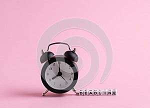 Black vintage alarm clock and cubes with letters with message deadline on a pink background