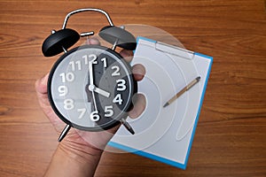 Black vintage alarm clock in hand with clipboard and blank white