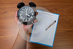 Black vintage alarm clock in hand with clipboard and blank white