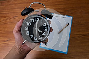 Black vintage alarm clock in hand with clipboard and blank white paper and pen, copy space for add your text, work on time or over
