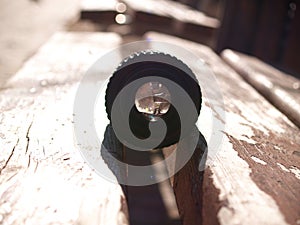 Black vintage lens lies on a wooden park bench, sun glare in reflection, sunny day