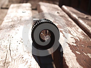 Black vintage lens lies on a wooden park bench, sun glare in reflection, sunny day