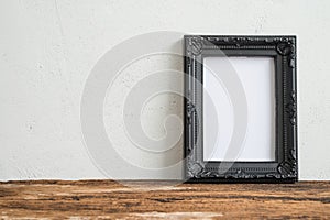 Black vintage photo frame on old wooden table over white wall ba