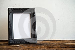 Black vintage photo frame on old wooden table over white wall ba