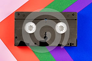 Black vintage VHS videotape on red, blue, green, purple and pink background. Plastic retro video cassette with analog