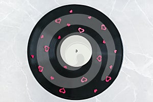 Black vinyl record covered with tiny red hearts on a marble background.