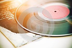 A black vinyl record lies on the cover of a music album, illuminated by sunlight