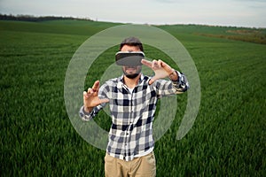 Black virtual reality glasses. Playing game. Handsome young man is on agricultural field