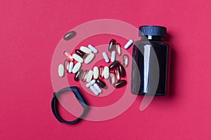 Black vitamin container, pills and fitnes tracker on red colored paper background