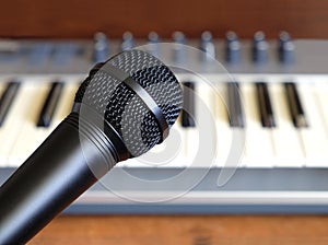 Black vocal microphone closeup against electronic synthesizer keyboard