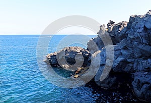 Black volcanic cliffs on the shores of the Mediterranean Sea in Italy. Catania, Sicily